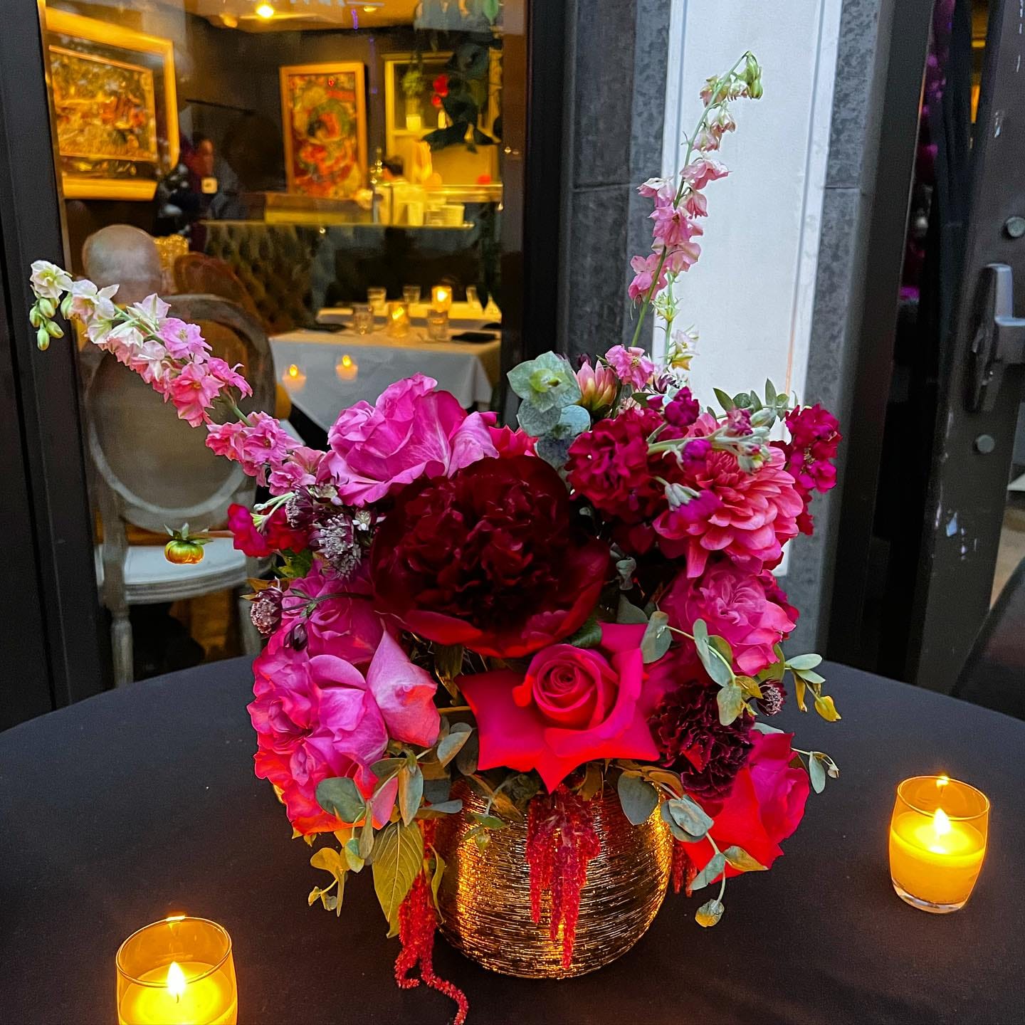 Hot-pink roses, burgundy peony and dahlia with votive candles on a dinner table