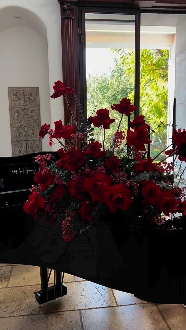 Red roses and hypericum berries spilling across the lid of a black grand piano