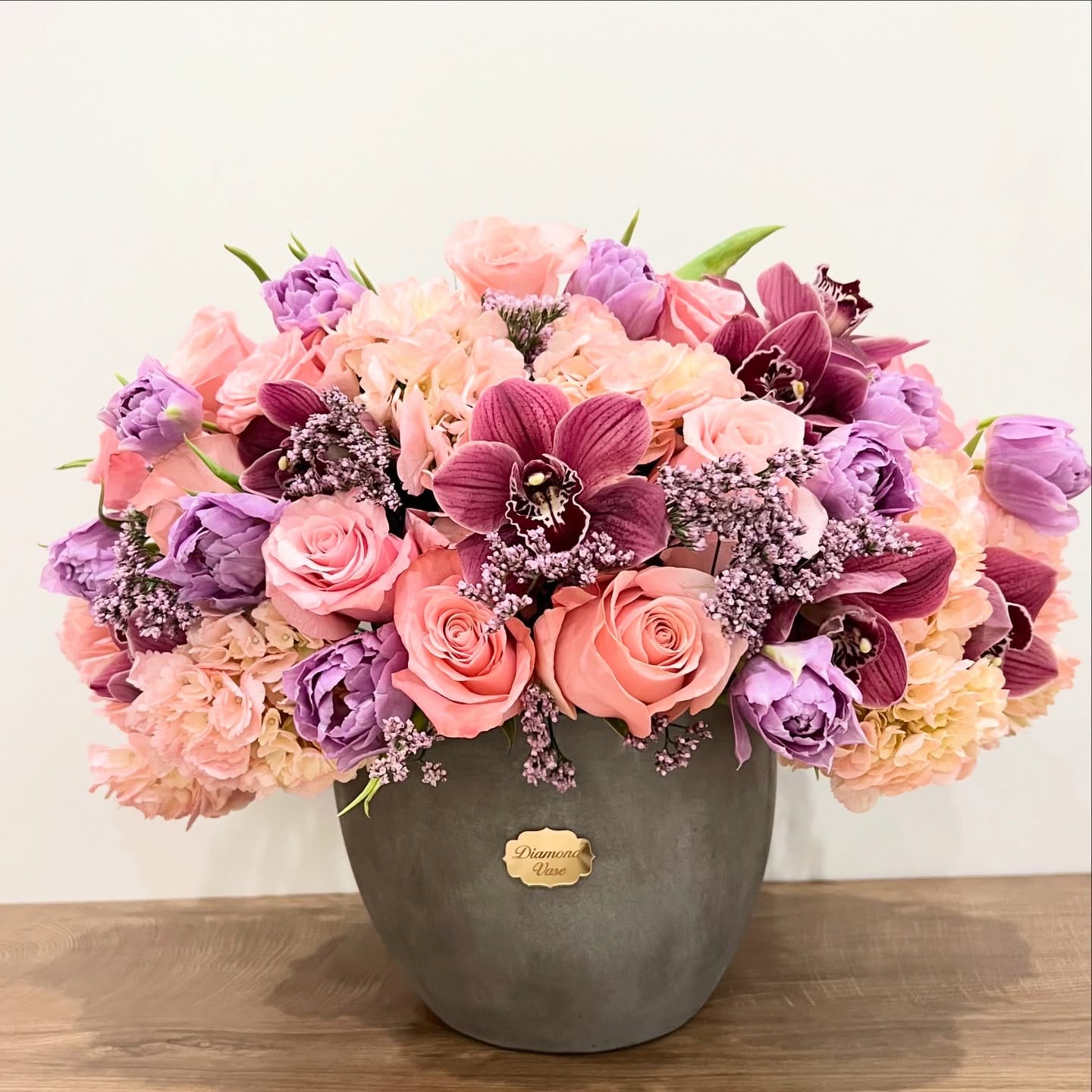 Peach roses, blush hydrangea, lavender tulips and cymbidium orchids in a grey concrete bowl