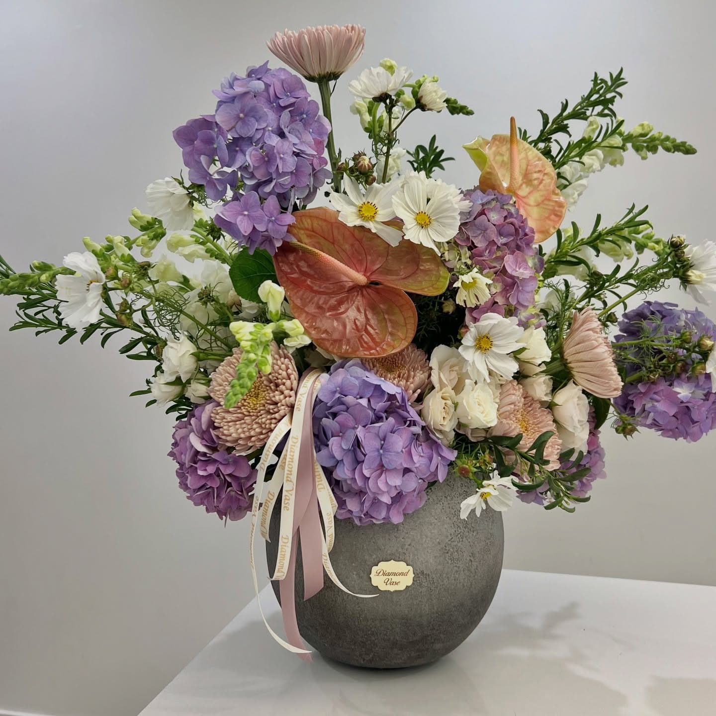 Lavender hydrangea, salmon anthurium, cosmos and snapdragons in a vase