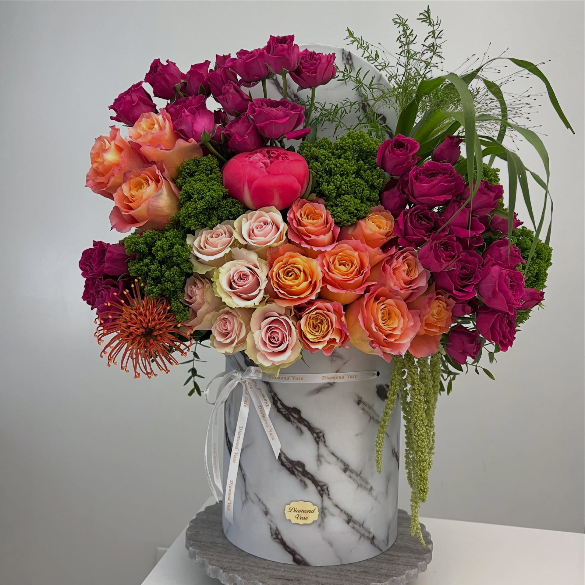 Magenta and coral roses, a hot-pink peony and orange protea in a marble-print Diamond Vase box