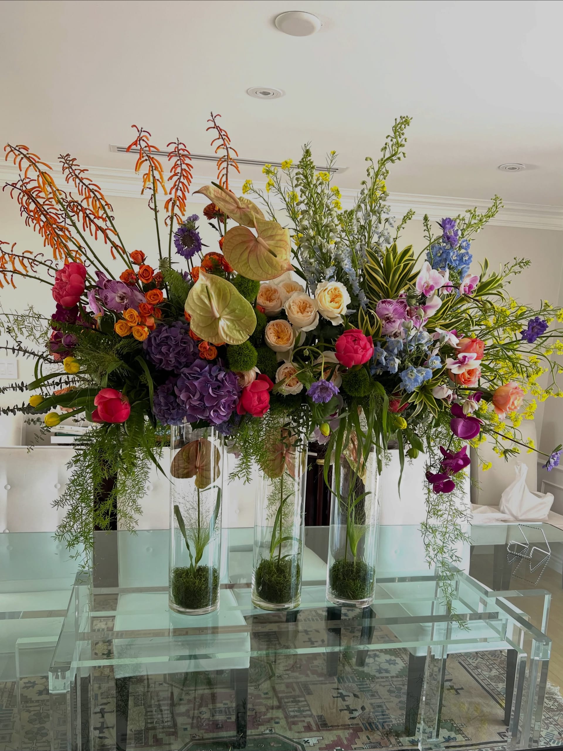 Tall, colorful arrangement in clear glass cylinders on a lucite table for a dessert-table celebration