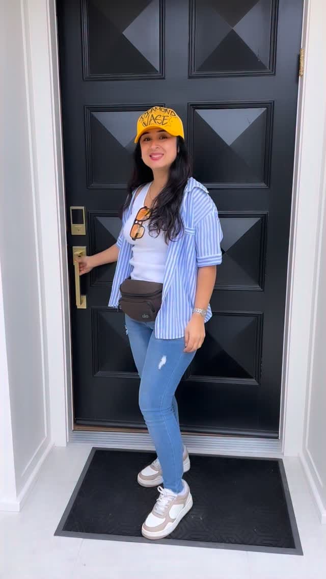Bita in a yellow Diamond Vase cap and blue striped shirt at a black paneled front door