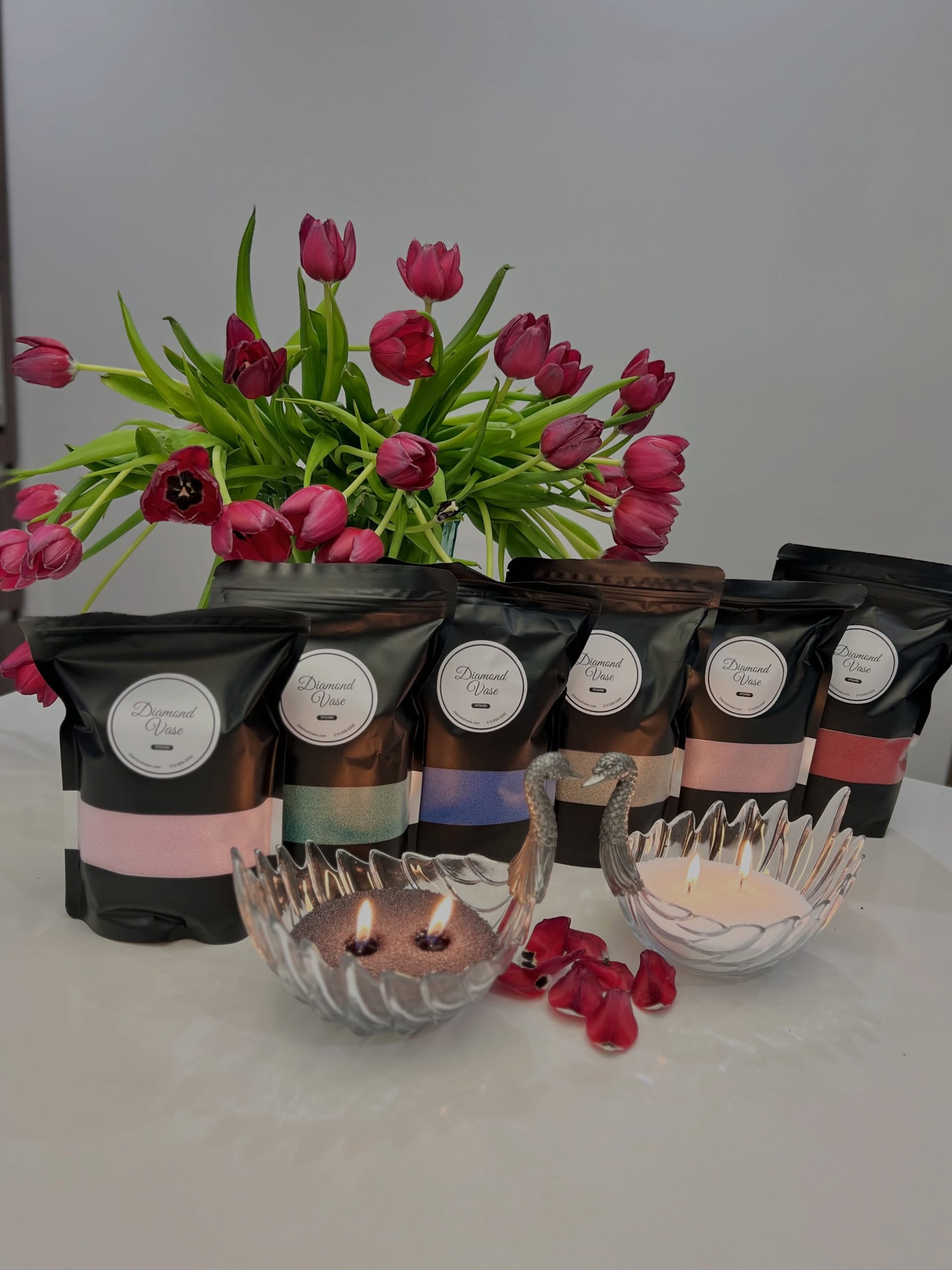 Glass swan bowls burning pink and white sand candles with magenta tulips, rose petals and black Diamond Vase pouches