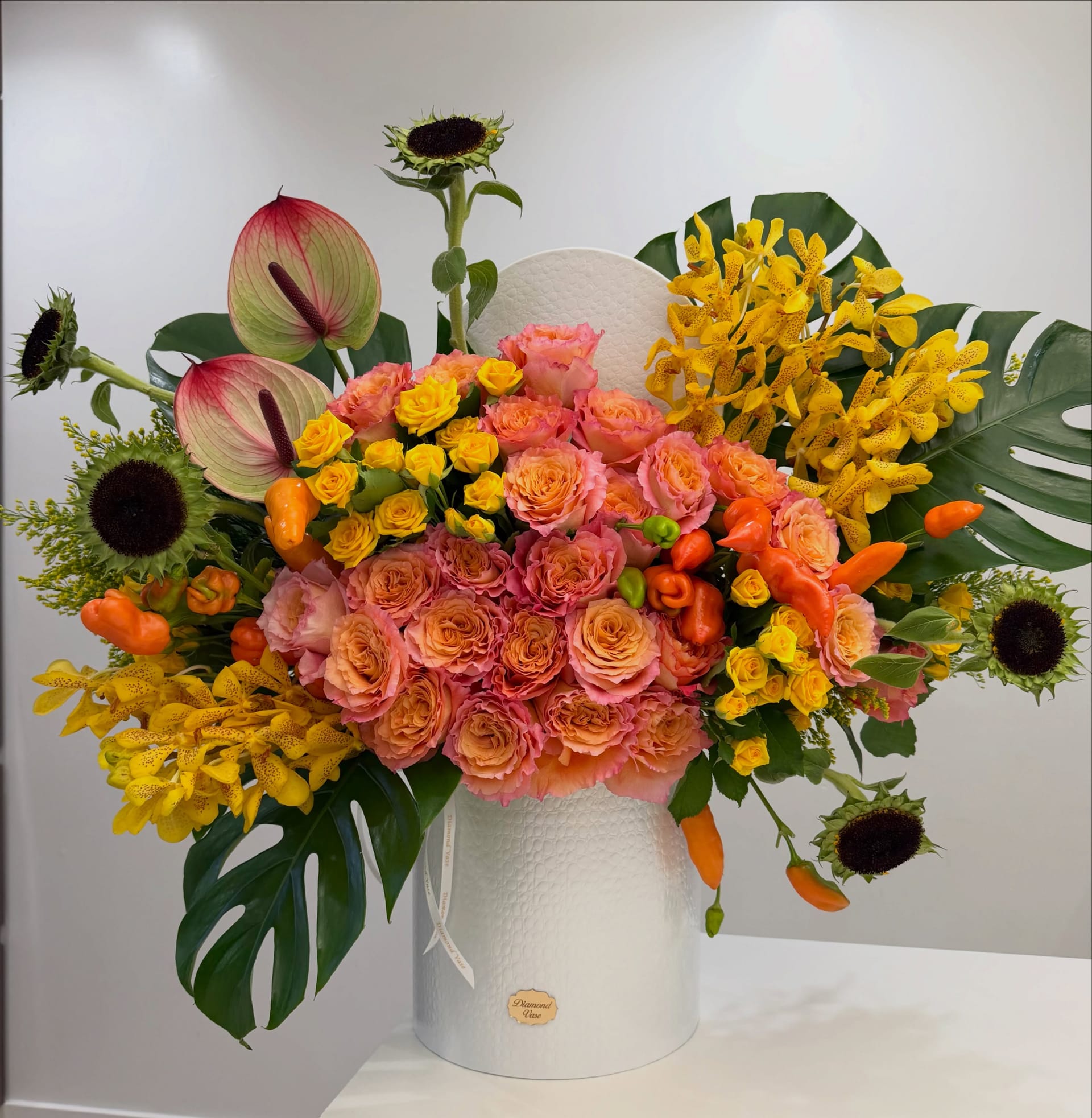 Orange garden roses, yellow spray roses, spotted orchids, anthurium and peppers in a white Diamond Vase box